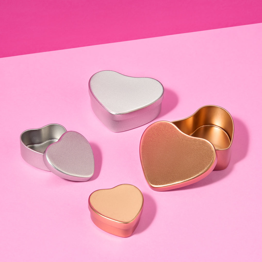 Collezione di barattoli a forma di cuore in argento e oro rosa su sfondo rosa